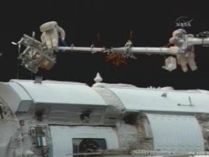 Här syns de två kosmonauterna i varsin ända av Strela. Längst ut till vänster på robotarmen syns plattformen som skyddspanelerna är fastspända på.